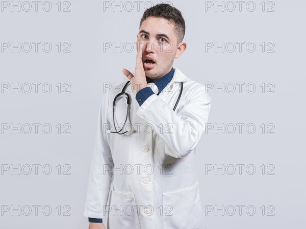 Young doctor whispering a secret on isolated background. Handsome doctor telling a gossip isolated, Doctor telling a secret