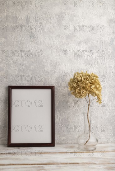 Brown wooden frame mockup with dried hydrangea in glass on gray concrete background. Blank, vertical orientation, still life, copy space