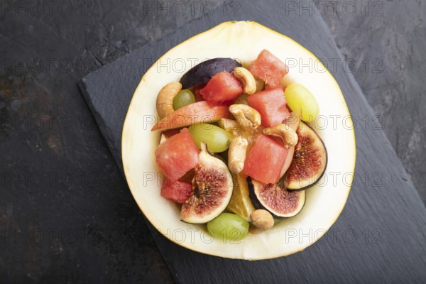 Vegetarian fruit salad of watermelon, grapes, figs, pear, orange, cashew on slate board on a black concrete background. Top view, flat lay, close up