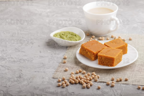 Traditional indian candy burfi in white plate with mint chutney on a gray concrete background. side view, copy space