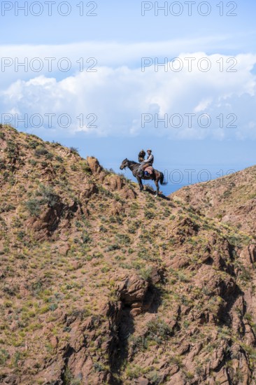 Traditional Kyrgyz eagle hunter with eagle in the mountains, hunting on horseback in front of dry landscape, near Kysyl-Suu, Issyk Kul, Kyrgyzstan, Asia