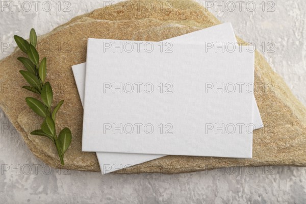 White paper business card, mockup with natural stone and boxwood branch on gray concrete background. Blank, flat lay, top view, still life, canvas, copy space