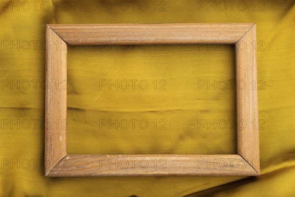 Wooden frame on smooth yellow silk tissue. Top view, flat lay, natural textile background and texture