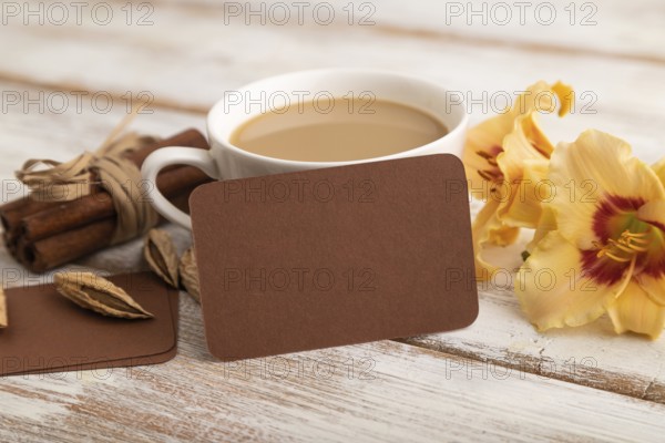 Brown paper business card mockup with orange day-lily flower and cup of coffee on white wooden background. Blank, side view, copy space, still life. spring concept