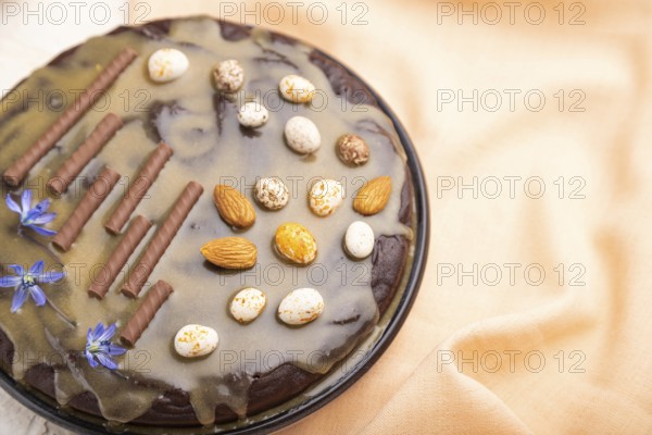 Homemade chocolate brownie cake with caramel cream and almonds with cup of coffee on a white concrete background and orange textile. Side view, close up, selective focus