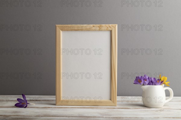 Beige wooden frame mockup with snowdrop crocus flowers on gray paper background. Blank, vertical orientation, still life, copy space