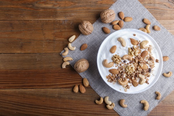 White plate with greek yogurt, granola, almond, cashew, walnuts on brown wooden background. top view. copy space