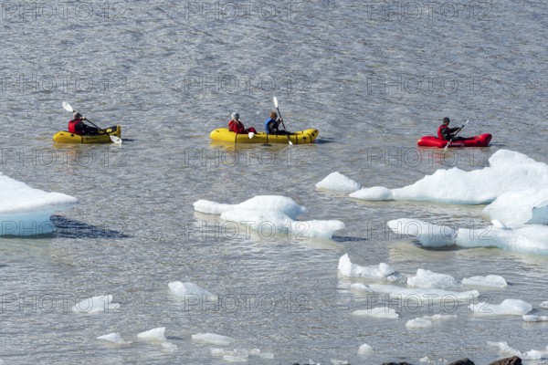 A group of tourists paddles in kayaks between icebergs, glacial lake Fjallsárlón, glacier Fjallsjökull, part of Vatnajökull glacier, Iceland, Europe