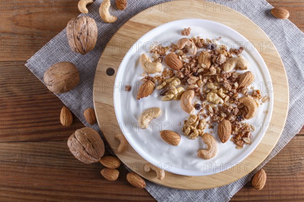 White plate with greek yogurt, granola, almond, cashew, walnuts on brown wooden background. top view