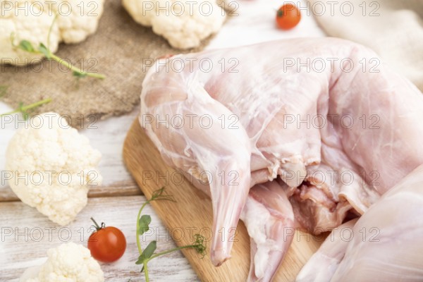 Whole raw rabbit with cauliflower, tomatoes and spices on a white wooden background and linen textile. Side view, close up, selective focus