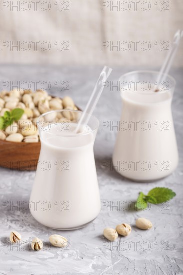 Organic non dairy pistachio milk in glass and wooden plate with pistachio nuts on a gray concrete background. Vegan healthy food concept, close up, side view