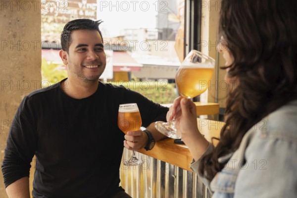 Smiling young man and woman enjoying a refreshing glass of beer at a daytime bar. The casual and lively atmosphere captures the joy of their social outing, creating a warm and inviting scene