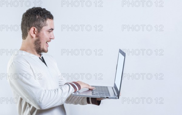 Portrait of happy young man standing using laptop isolated. Excited guy holding and looking at an promotion on laptop screen