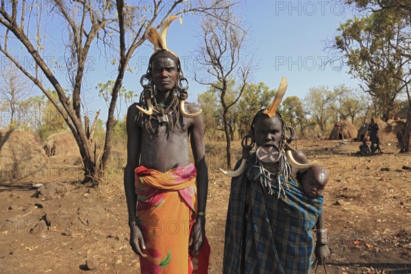 Southern Ethiopia, in Maco National Park, Mursi tribe, Mursi man, Mursi woman with baby, painted skin and headdress, plate-lipped woman, woman with plate in lower lip, Ethiopia, Africa