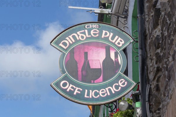 Traditional Dingle pub sign with wine bottles and glass attached to a stone façade under a blue sky, Dingle, Dingle Peninsula, County Kerry, Republic of Ireland