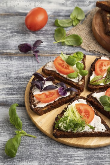 Grain rye bread sandwiches with cream cheese, tomatoes and microgreen on gray wooden background and linen textile. side view, close up