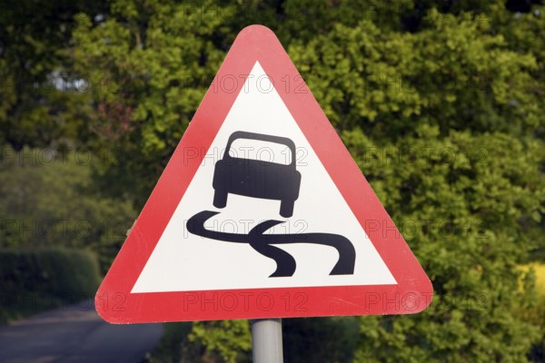 Red triangular road sign warning of slippery road