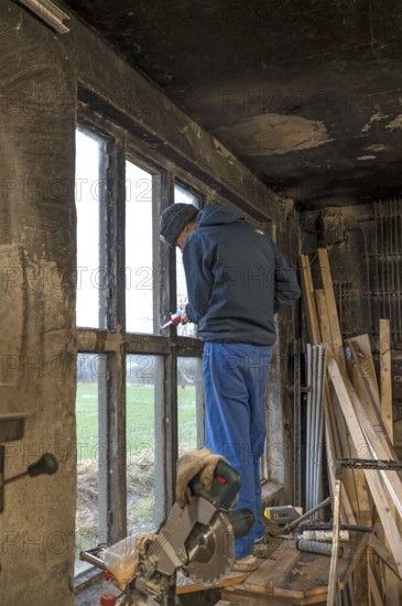 Young man in his workshop, standing on the workbench and repairing a window, Mecklenburg-Vorpommern, Germany, Europe