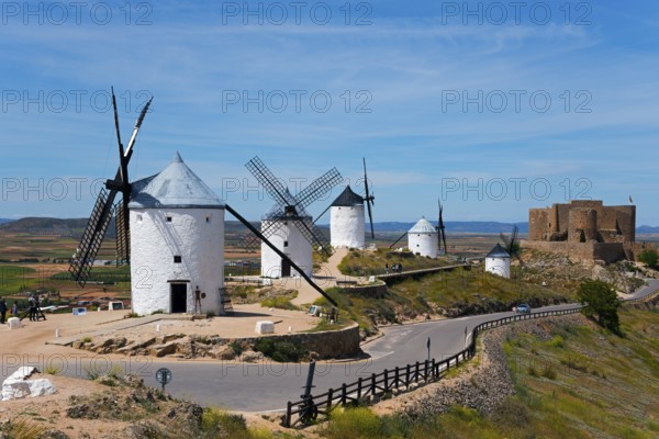 Several white windmills on a hill, with a castle in the background under a blue sky, Consuegra, Toledo, Castilla-La Mancha, Route of Don Quixote, Spain, Europe