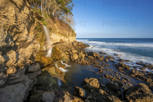 Waterfall falls into the sea on the cliffs, Catarata el Chorro, coastal landscape in the evening light, long exposure, Playa Cocalito, Pacific coast, Nicoya Peninsula, Puntarenas province, Costa Rica, Central America