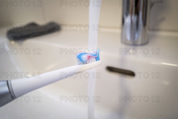 A bathroom tap is running while a toothbrush is held under the running water, symbolic image of water consumption