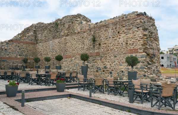 A street café in front of the ruins of an old wall under a partly cloudy sky in an urban historical area, Komotini, Eastern Macedonia and Thrace, Greece, Europe