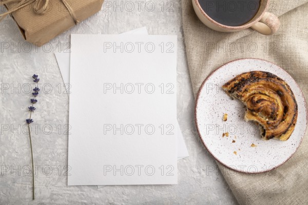 White paper invitation card, mockup with lavender, bun, cup of coffee, linen textile, box on gray concrete background. Blank, flat lay, top view, still life, copy space