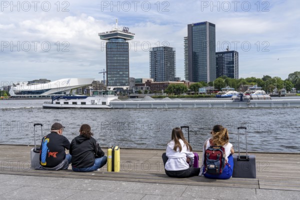 Tourists sitting at the back of Amsterdam Centraal railway station, on the promenade of the river Ij, A'DAM Lookout, skyscraper, sight, This is Holland, Amsterdam, Netherlands