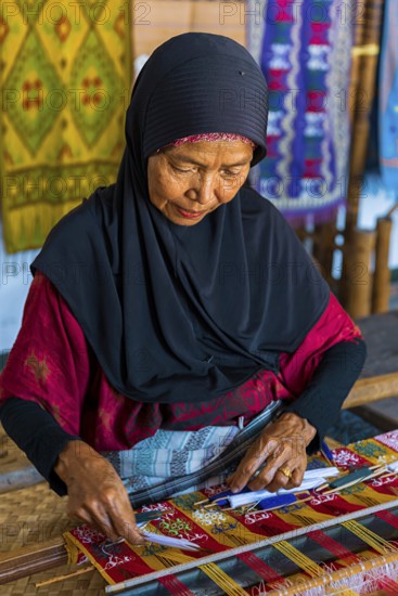 Traditional weaver, weaving, woman's work, working conditions, loom, textile, woman, trade, bazaar, authentic, fabric, fabric pattern, craft, handicraft, Asian, indigenous, tradition, traditional, marketplace, travel, tourism, culture, poverty, presentation, lifestyle, person, Muslim, Islam, Sasak, indigenous, indigenous people, cultural heritage, silk weaving, Sade village, Lombok, Indonesia, Asia