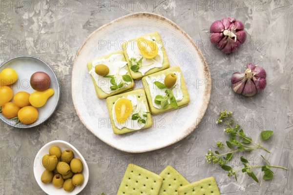 Green cracker sandwiches with cream cheese and cherry tomatoes on gray concrete background. top view, flat lay, close up