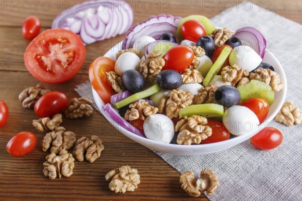 Salad with fresh cherry tomatoes, mozzarella cheese, olives, kiwi, onion and walnuts on brown wooden background, copy space, close up