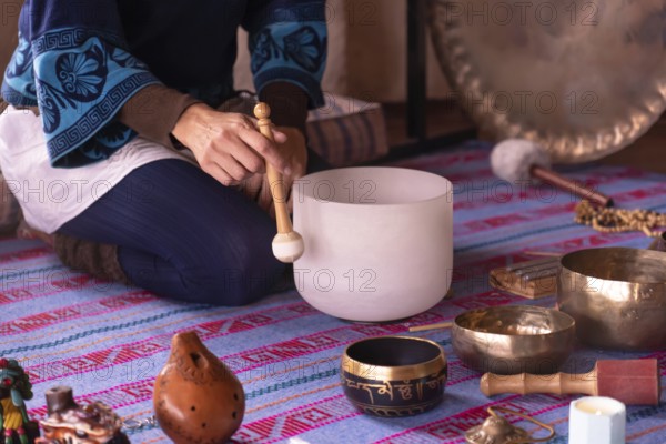 Close-up of a woman's hands playing a quartz singing bowl, while guiding a sound meditation surrounded by other instruments such as Tibetan singing bowls and a gong