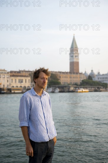 Young man in striped shirt and shorts on the banks of the Grand Canal, behind Campanile, Venice, Veneto, Italy, Europe