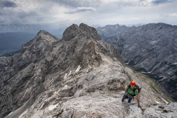 Mountaineer with helmet climbing on the rock, on a narrow rocky ridge, crossing the Jubiläumsgrat, view of the Rhine valley and Alpspitze, Wetterstein range, Bavaria, Germany, Europe