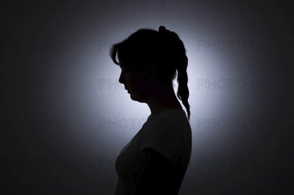 Symbolic photo on the subject of loneliness in woman. The silhouette of a young woman stands out against a white wall. Berlin, 22.08.2024