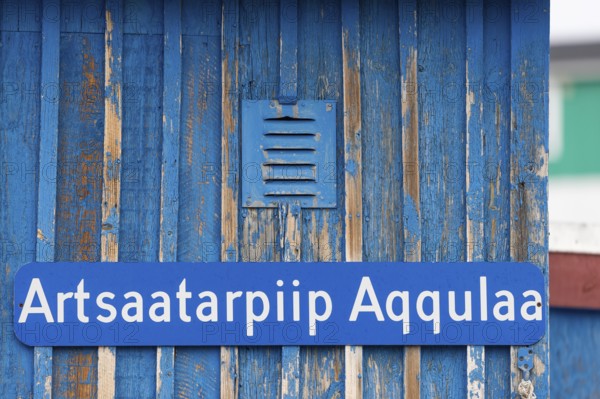 A blue sign inscribed with a Greenlandic street name on a weather-beaten wooden wall, remote Arctic Inuit settlement of Ittoqqortoormiit, Scoresbysund or Scoresby Sund or Greenlandic Kangertittivaq, East Greenland, Greenland, North America