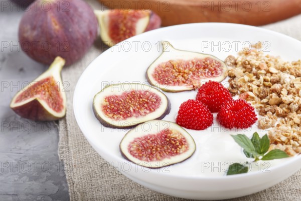 Yoghurt with raspberry, granola and figs in white plate on a gray concrete background and linen textile. side view, close up, selective focus