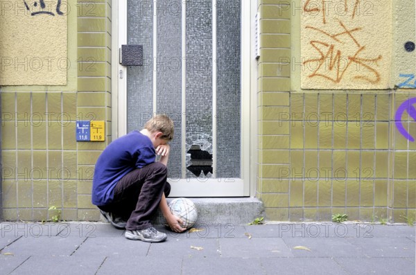 Crying ten-year-old boy Ten-year-old in front of the smashed glass pane on a front door, Germany, Europe