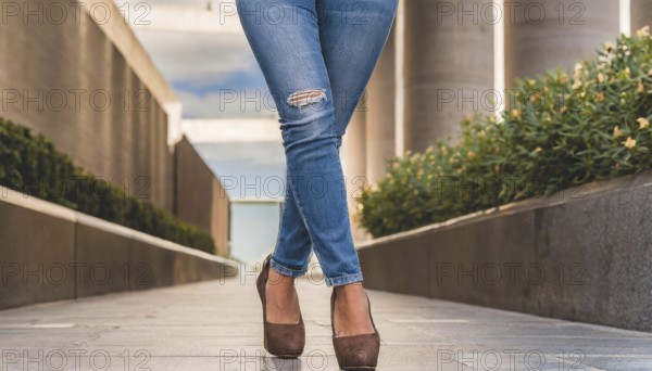 A person in jeans and brown high heels stands in a modern urban environment on a sunny day, AI generated, AI generated