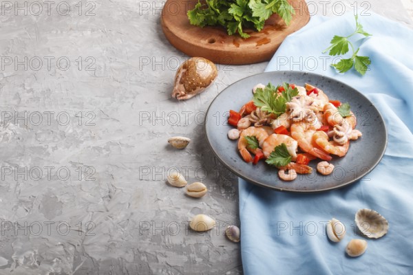 Boiled shrimps or prawns and small octopuses with herbs on a blue ceramic plate on a gray concrete background and blue textile. Side view, copy space