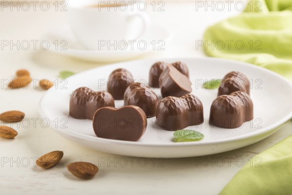 Chocolate candies with almonds and a cup of coffee on a white wooden background and green textile. side view, close up, selective focus