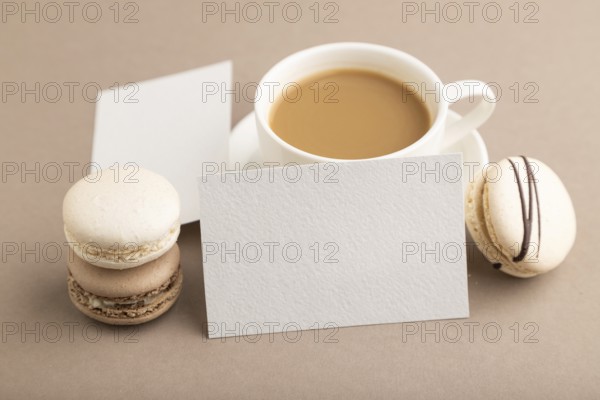 White paper business card mockup with brown and white macaroons and cup of coffee on beige pastel background. Blank, side view, copy space, still life, close up. morning, breakfast concept