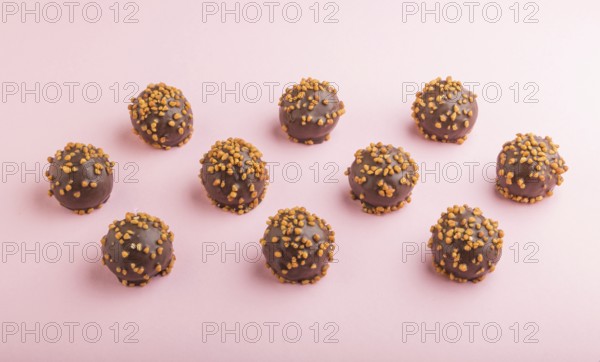 Chocolate caramel ball candies with almonds in a row on a pastel pink background. side view, close up