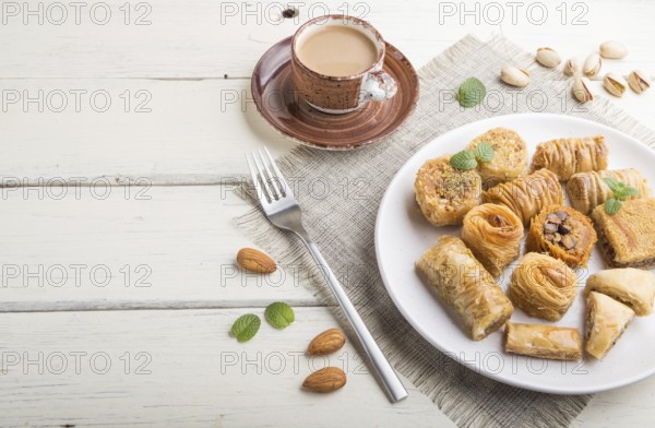 Traditional arabic sweets (kunafa, baklava) and a cup of coffee on a white wooden background and linen textile. side view, copy space