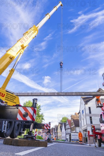 A yellow lifting crane on a busy construction site under a blue sky with buildings in the background, Hermann Hesse railway construction site, Calw, Black Forest, Germany, Europe