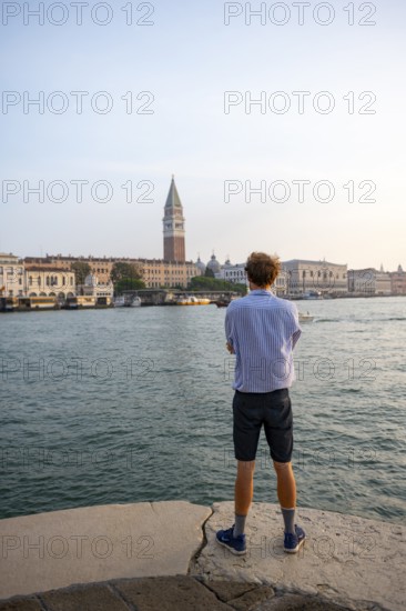 Young man in striped shirt and shorts on the banks of the Grand Canal, behind Campanile, Venice, Veneto, Italy, Europe