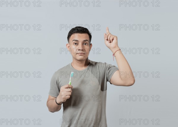 Handsome guy holding toothbrush pointing an advertisement up. Caucasian handsome man holding toothbrush pointing up. People holding toothbrush pointing a promo up