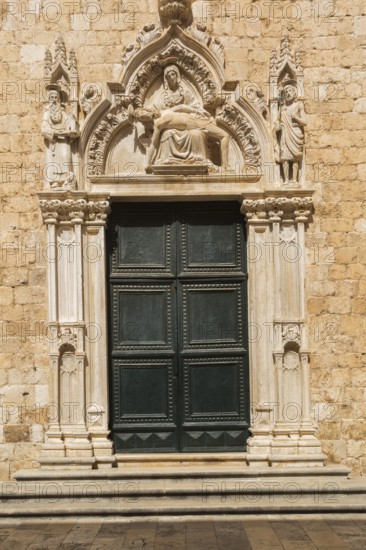 Ornate dark green entrance door decorated with carved religious figures at Franciscan Monastery, Old walled city of Dubrovnik, Croatia, Europe