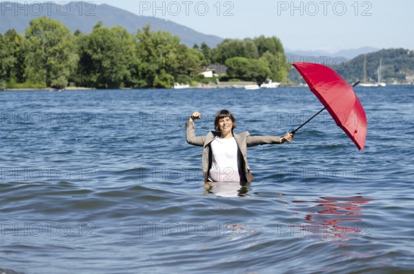 Elegant Business Woman with Suit Standing in the Water and Holding a Red Umbrella