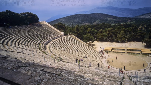 People explore the extensive ruins of an ancient amphitheatre with mountain views, Ancient Amphitheatre, Epidaurus, Peloponnese, Greece, Europe